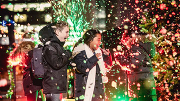 Three children smiling in the middle of snow and backlit by green and red lights