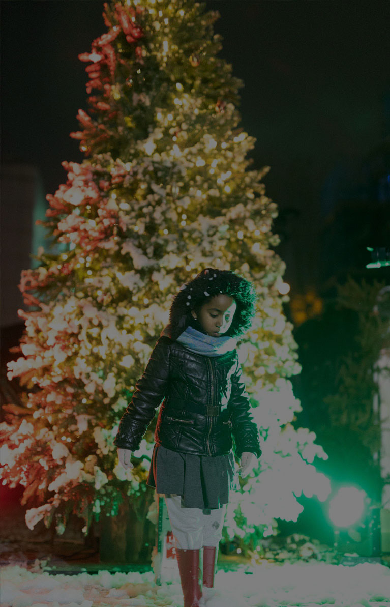 Young girl standing in snow and in front of a christmas tree