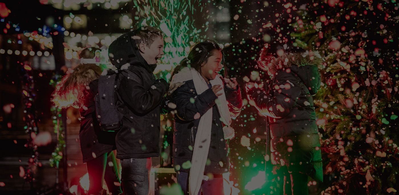Three children smiling in the middle of snow and backlit by green and red lights